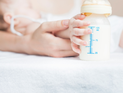 Infant holding a bottle of baby formula.